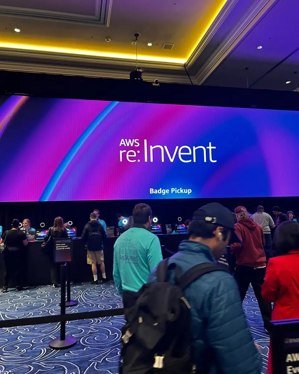 Pantalla de AWS re:Invent en la zona de registro de badges, con asistentes haciendo fila