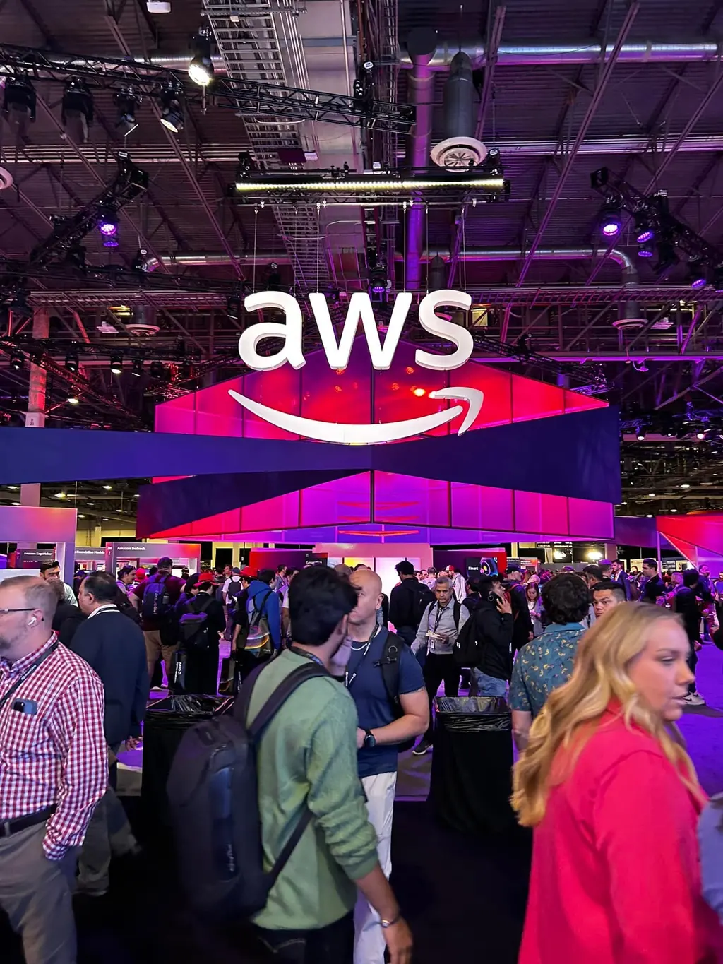 Expo hall de AWS re:Invent con el gran letrero de AWS iluminado y asistentes recorriendo los stands